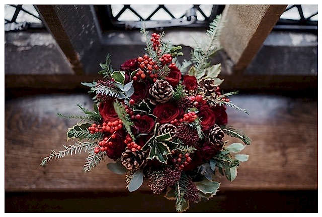 Christmas wedding, bridal hand-tied winter bouquet with deep red Grand Prix roses, burgundy roses, spray roses, ilex berries, hypericum berries, pine cones, eucalyptus and for and holly.